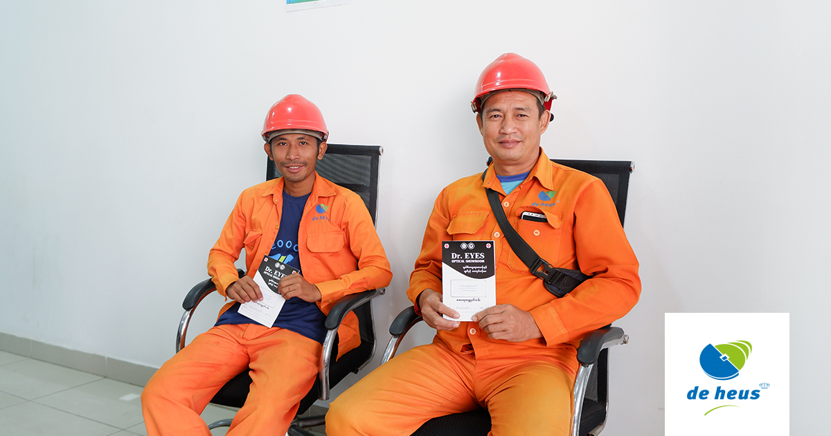 two factory workers are sitting on the chairs and holding booklets.