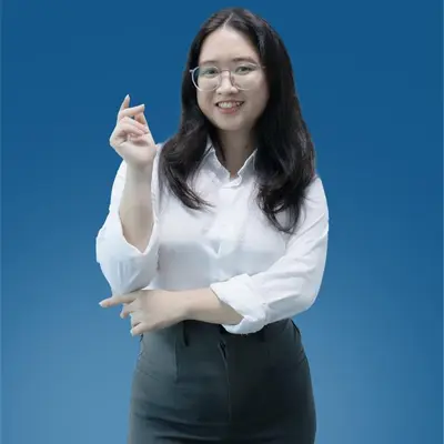 A girl who is wearing a eyeglasses is standing and smiling and looking at the camera.
