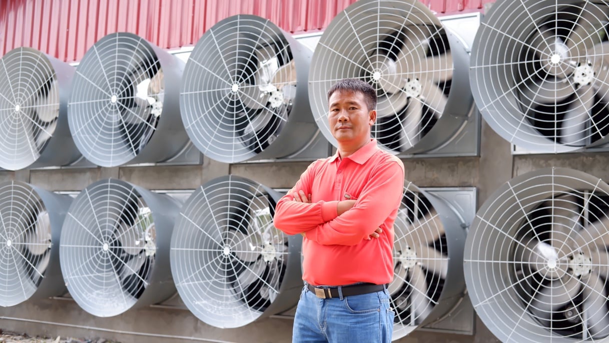 a man standing in front of the large exhaust fans at a farm